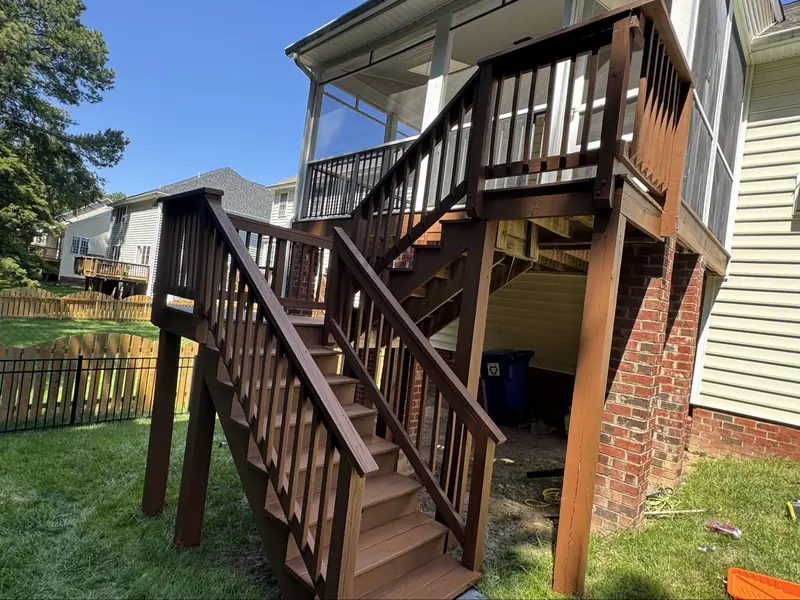 Tall stained deck with full staircase and railings below a screened porch